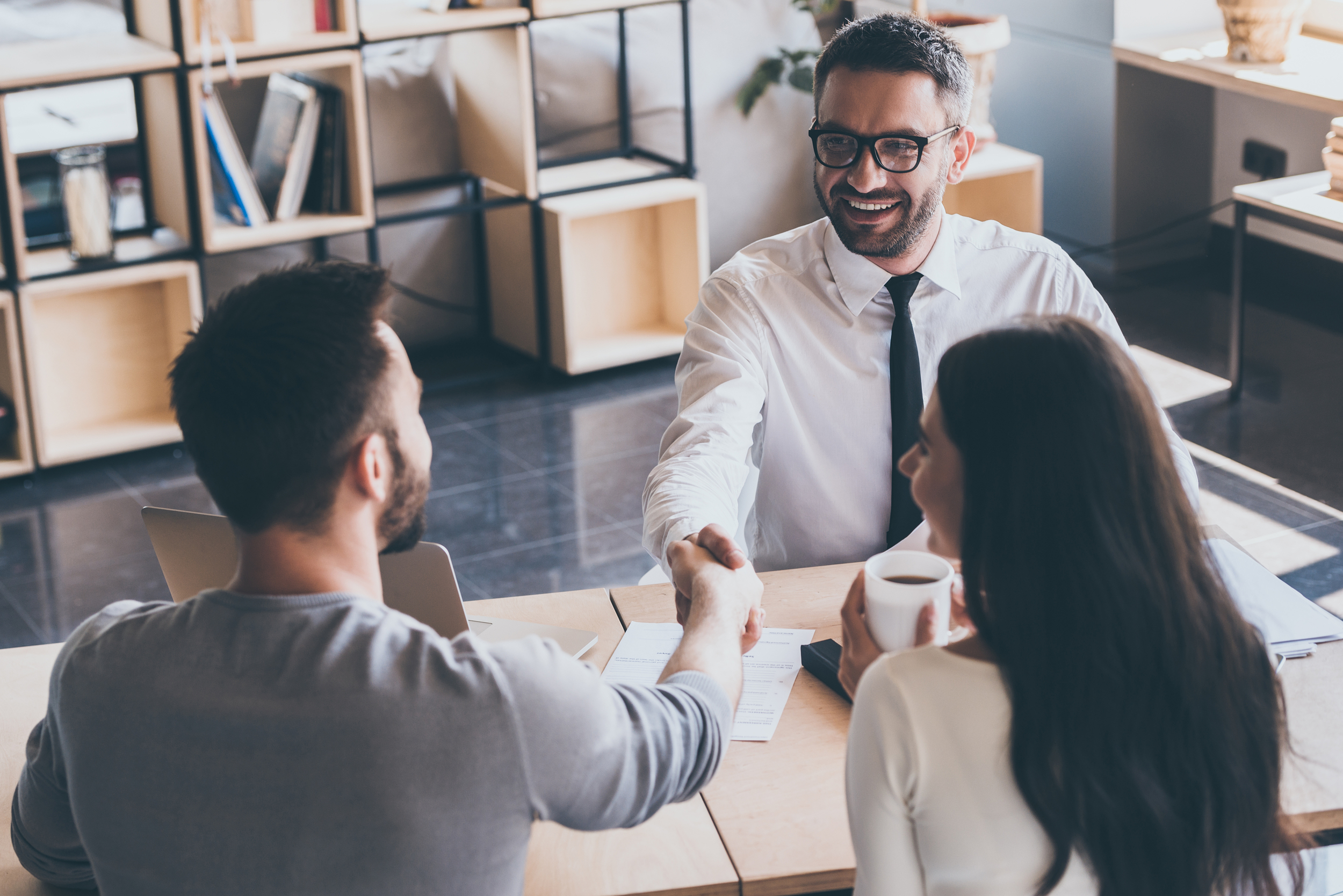 Three people in an office, with two men shaking hands