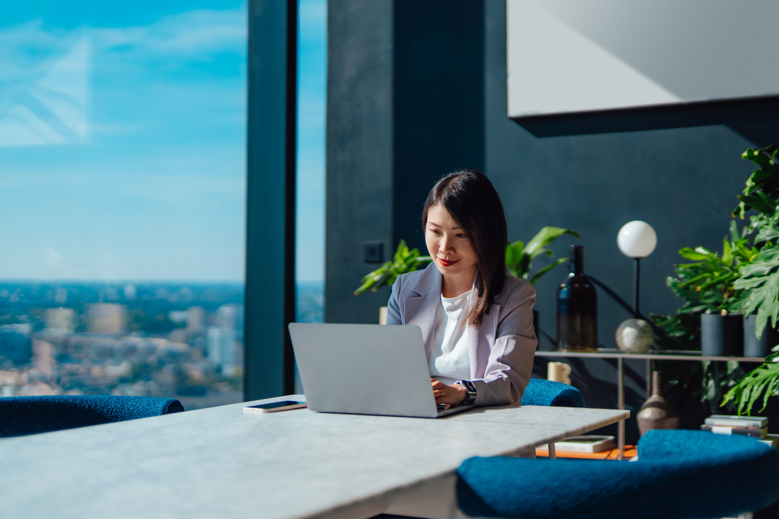 Lady looking at a laptop screen on a table beside a glass wall.